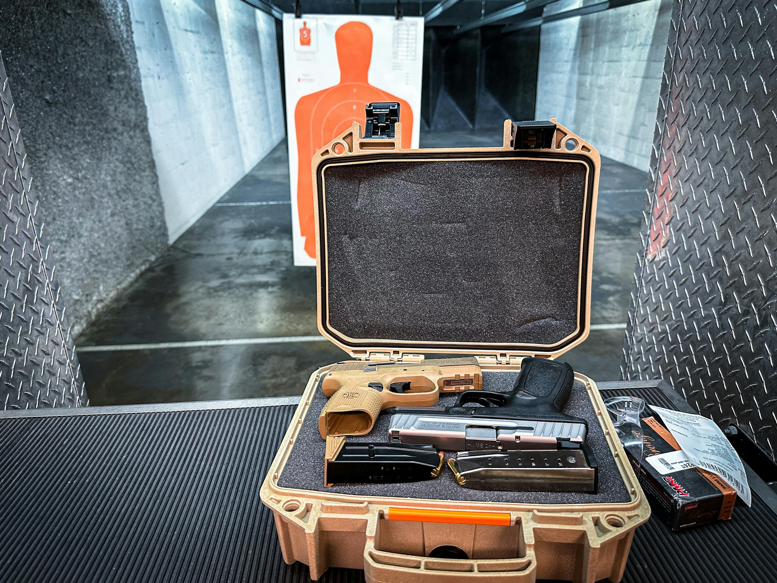Open handgun case with firearm and accessories at an indoor shooting range.